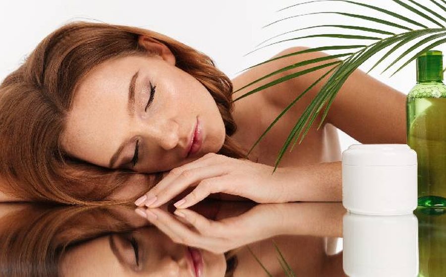 A woman resting her head on her arms beside skincare bottles