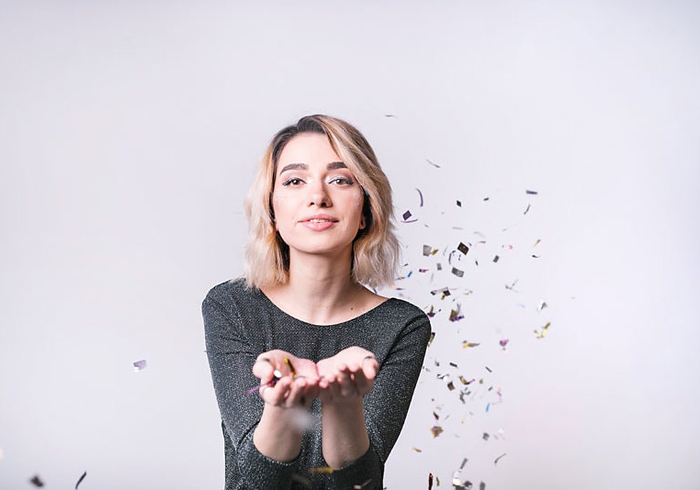 A smiling woman blowing confetti from her hands